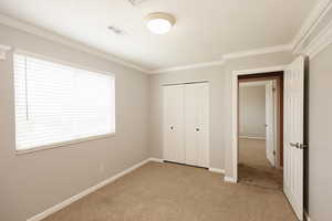 Unfurnished bedroom featuring light carpet, a closet, and crown molding