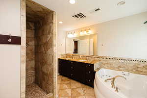 Bathroom with double vanity, a jetted tub, tile walls, a walk in shower, and light tile patterned floors