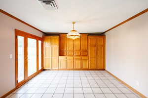 Unfurnished dining area with ornamental molding, hanging lights, and light tile patterned floors