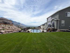 Expansive green lawn with a retaining wall, a fenced in-ground pool, and a stucco exterior featuring multiple windows