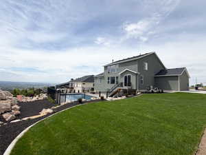 Expansive backyard featuring a manicured lawn, a fenced-in swimming pool, a multi-level deck with black railings, and a rock garden with dark ground cover