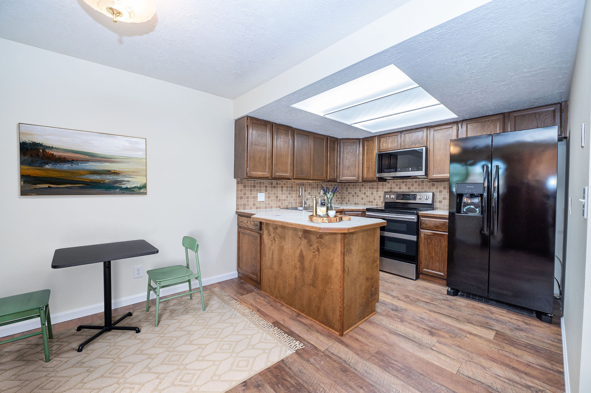 Kitchen featuring wood-finish flooring, wood cabinetry, a light-toned backsplash, a central island with a solid surface countertop, and a skylight