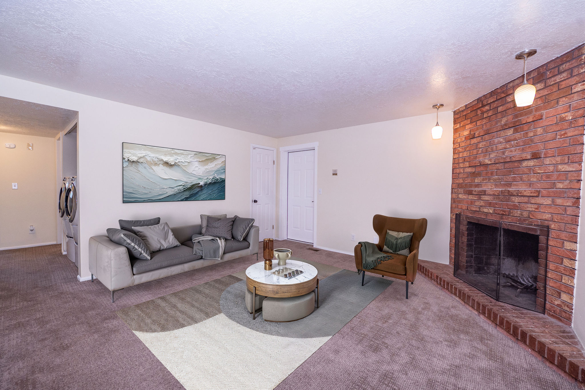 Living area featuring a brick fireplace with a raised hearth, recessed screen, and dual pendant lighting fixtures