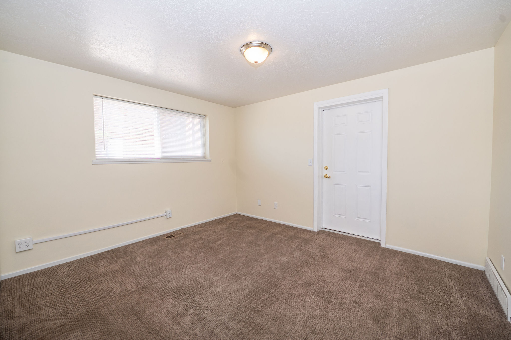 Neutral tone wall paint, brown carpeting, a window with blinds, a white paneled door, and a flush mount ceiling light fixture