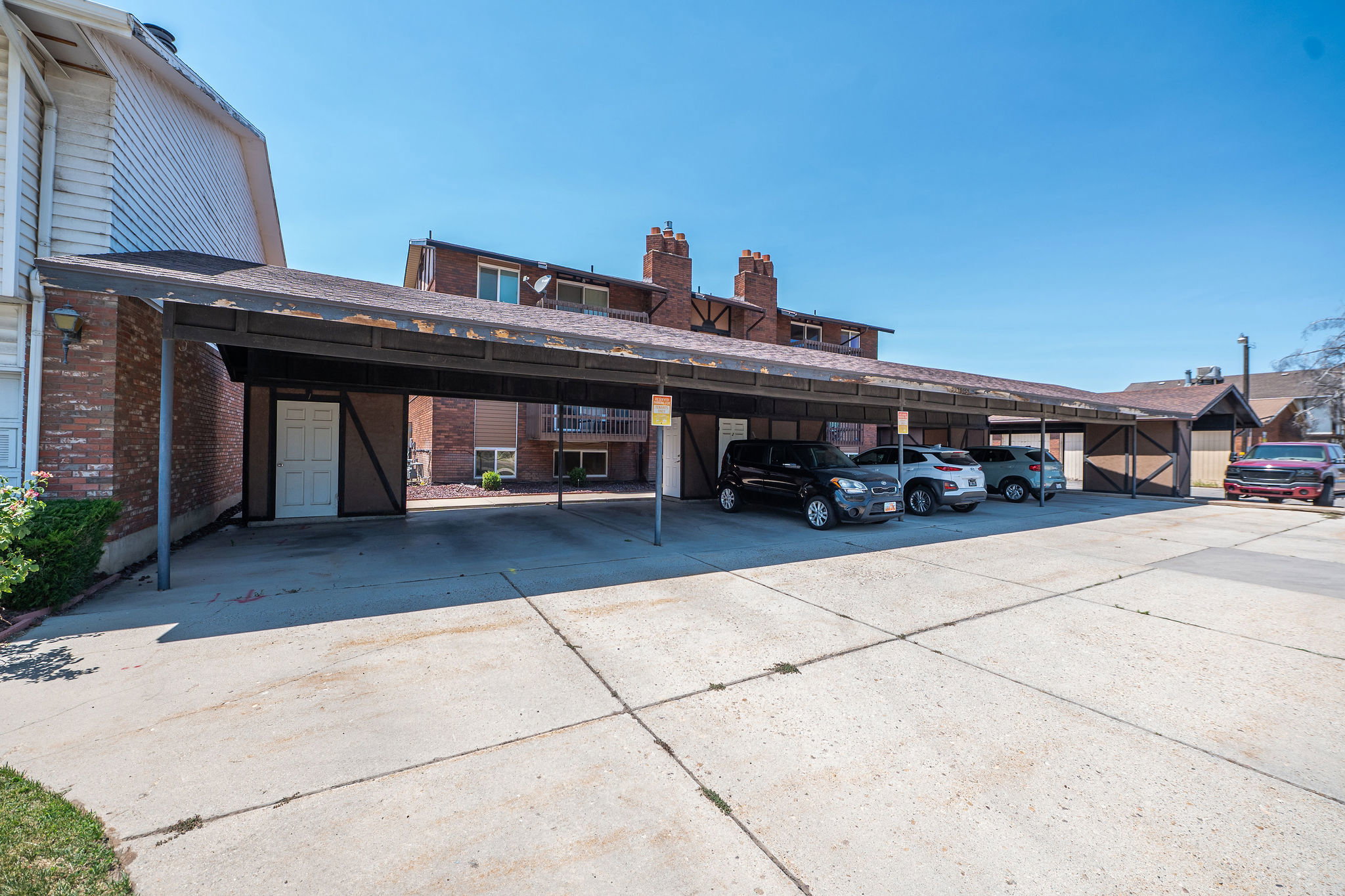 Covered parking structure with multiple spaces, featuring a sloped roof and supporting metal posts