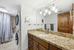 Bathroom with vanity, light tile patterned flooring, stacked washer and clothes dryer, and shower / tub combo