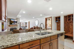 Kitchen featuring open floor plan, wood finish cabinetry, ceiling fan, light stone counters, and a stone fireplace