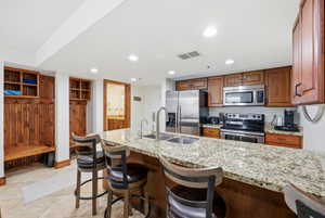 Kitchen featuring wood finish cabinets, light stone counters, a breakfast bar area, stainless steel appliances, and recessed lighting