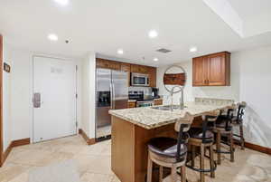 Kitchen with a kitchen bar, a peninsula, wood finish cabinetry, stainless steel appliances, and recessed lighting
