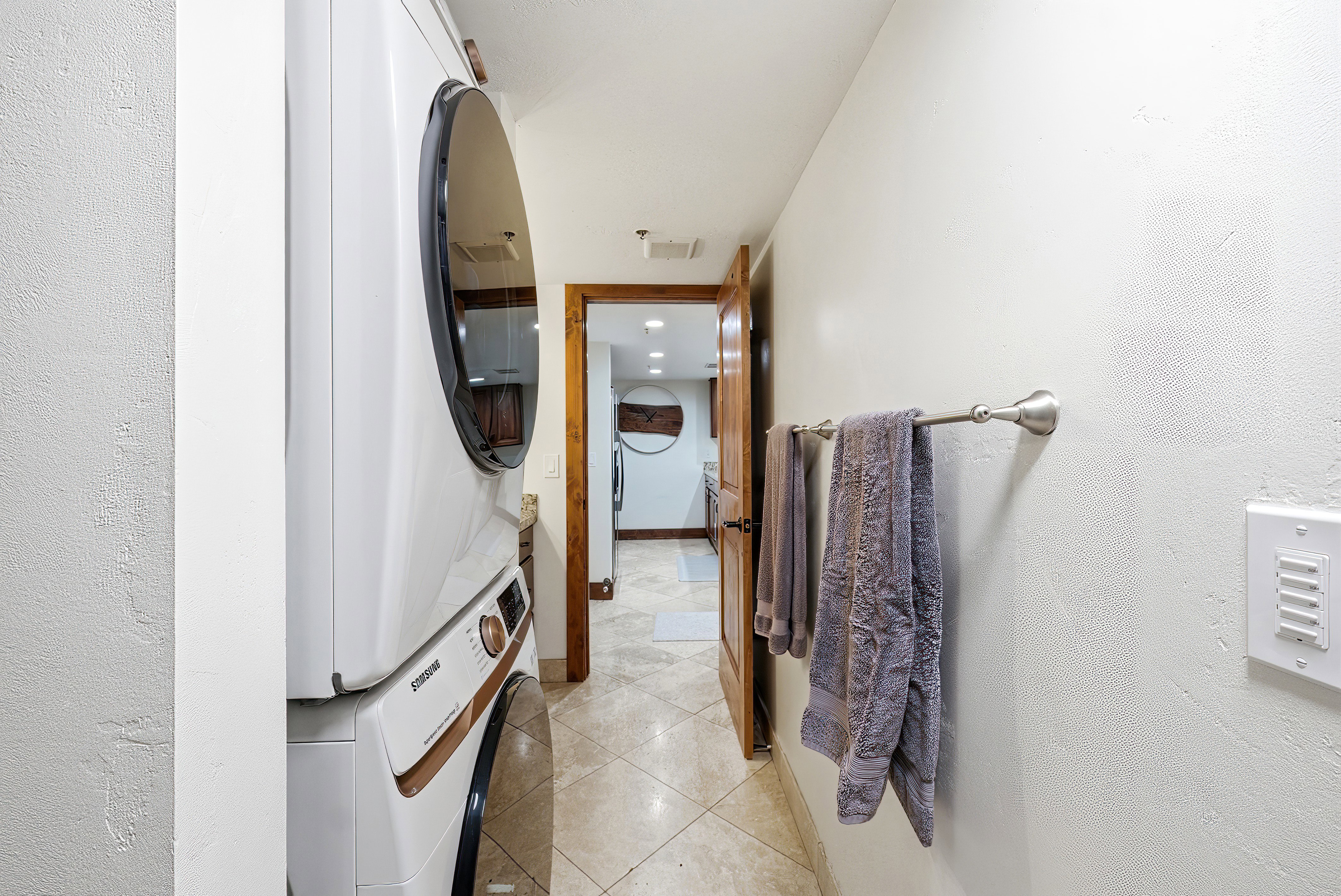 Laundry area with light tile patterned floors, stacked washing machine and dryer, recessed lighting, and a textured wall