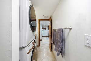 Laundry area with light tile patterned floors, stacked washing machine and dryer, recessed lighting, and a textured wall