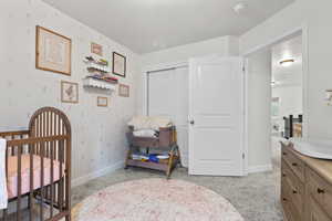 Bedroom featuring light carpet, a nursery area, and a closet