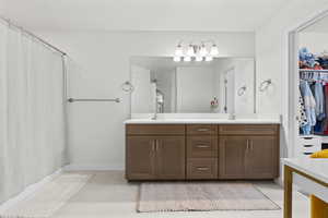 Bathroom with double vanity, curtained shower, a walk in closet, and light tile patterned flooring