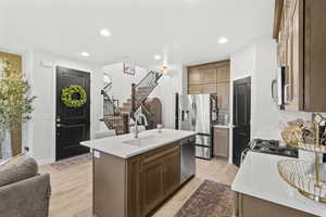 Kitchen featuring a kitchen island with sink, light wood-style floors, light stone countertops, stainless steel appliances, and recessed lighting