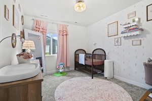 Bedroom featuring wallpapered walls, light colored carpet, and a nursery area