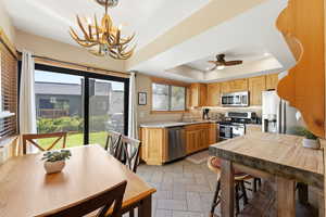 Kitchen featuring light countertops, stainless steel appliances, a tray ceiling, a chandelier, and light wood finish cabinetry