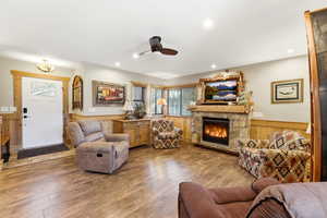 Living room with wainscoting, ceiling fan, a fireplace, wood walls, and wood-type flooring