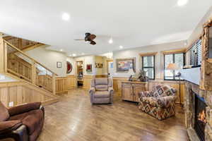 Living area featuring wainscoting, wood-type flooring, ceiling fan, a fireplace, and wooden walls