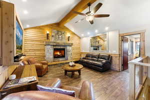 Living area with a fireplace, beamed ceiling, wooden walls, wood-type flooring, and a ceiling fan