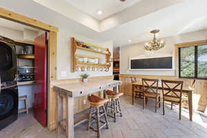Bar with stacked washing machine and dryer, open shelves, and a chandelier