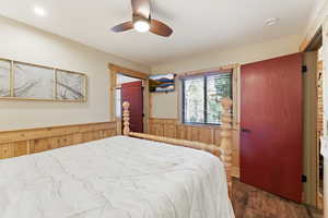 Bedroom with wooden walls, dark wood finished floors, a wainscoted wall, and a ceiling fan