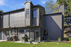 Rear view of property featuring a chimney, a lawn, and a patio