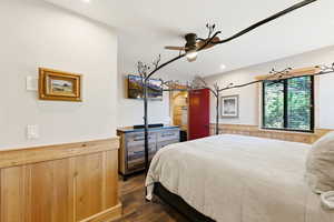 Bedroom with dark wood-style floors, wooden walls, wainscoting, ceiling fan, and recessed lighting