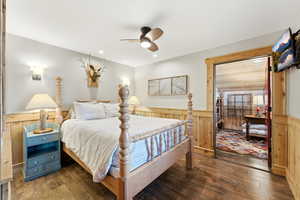 Bedroom featuring hardwood / wood-style floors, ceiling fan, wainscoting, and wood walls