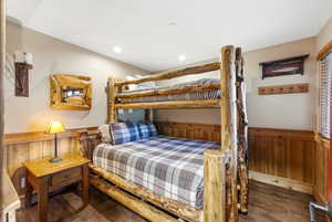 Bedroom featuring wooden walls, wainscoting, and dark wood-style floors