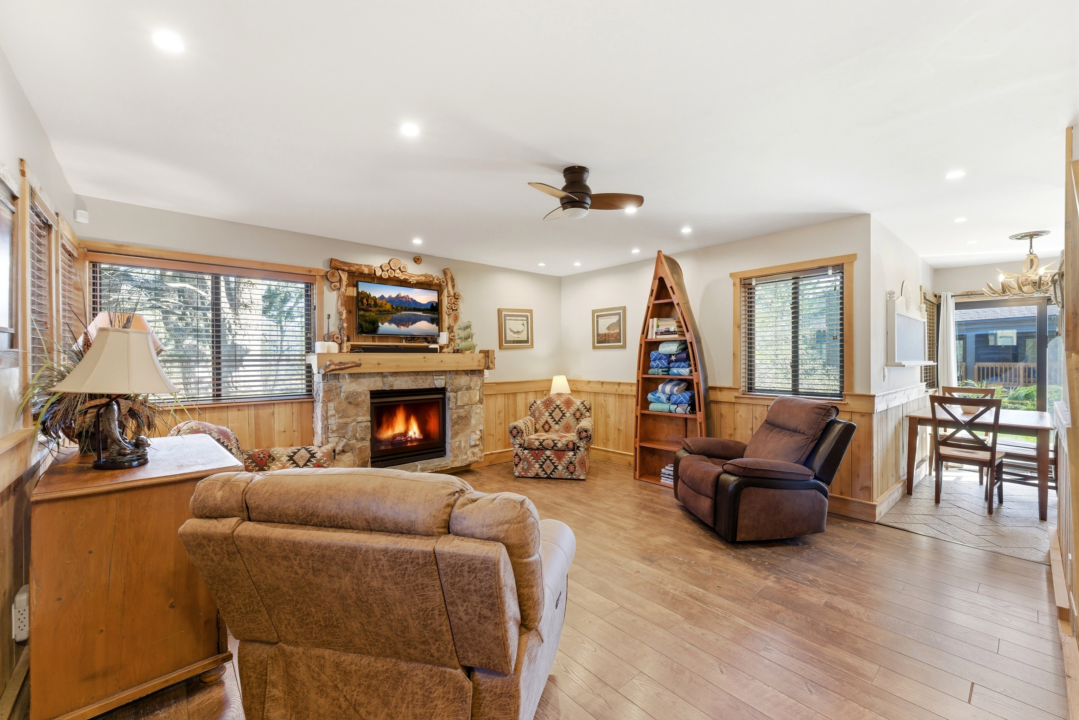 Living area featuring a wainscoted wall, a stone fireplace, a ceiling fan, wood walls, and light wood finished floors