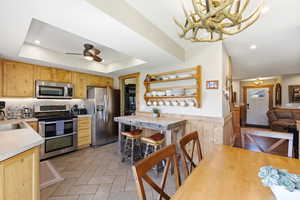 Kitchen featuring light wood finish cabinetry, light countertops, stainless steel appliances, a wainscoted wall, and decorative light fixtures