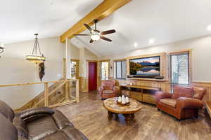 Living area featuring wainscoting, hardwood / wood-style flooring, ceiling fan, beam ceiling, and wooden walls