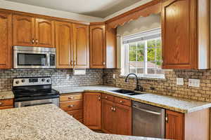Kitchen with stainless steel appliances, light stone counters, wood finish cabinetry, and tasteful backsplash