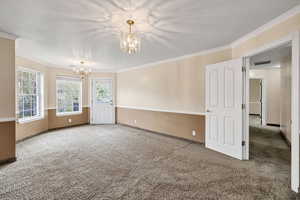 Carpeted spare room featuring suspended lighting, a textured ceiling, and ornamental molding