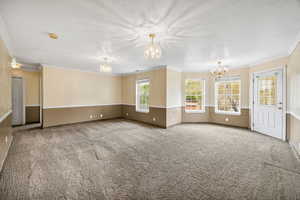 Unfurnished living room with a chandelier, carpet flooring, crown molding, and a textured ceiling