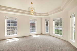 Unfurnished room featuring a chandelier, carpet flooring, and a raised ceiling