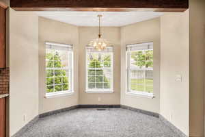 Unfurnished dining area with carpet floors, a chandelier, and beam ceiling
