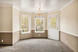Unfurnished dining area with light carpet, a chandelier, a textured ceiling, and crown molding