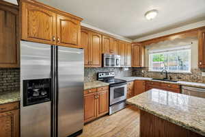 Kitchen with stainless steel appliances, light stone counters, light wood-style flooring, and wood finish cabinetry