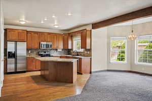 Kitchen with stainless steel appliances, wood finish cabinetry, light stone countertops, a kitchen island, and beamed ceiling