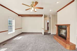 Unfurnished living room featuring ceiling fan, carpet, a tile fireplace, and ornamental molding