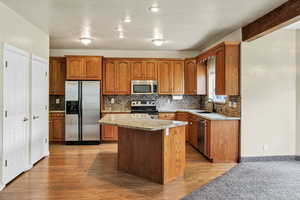Kitchen with stainless steel appliances, light stone counters, wood finish cabinetry, and light wood-type flooring