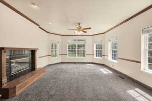 Unfurnished living room with carpet floors, a glass covered fireplace, a ceiling fan, and ornamental molding