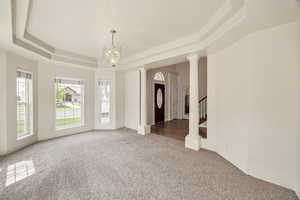 Empty room featuring a raised ceiling, suspended lighting, light colored carpet, and decorative columns
