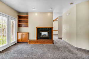 Unfurnished living room featuring a tiled fireplace and carpet flooring