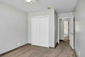 Unfurnished bedroom with carpet floors, a textured ceiling, a closet, and a ceiling fan