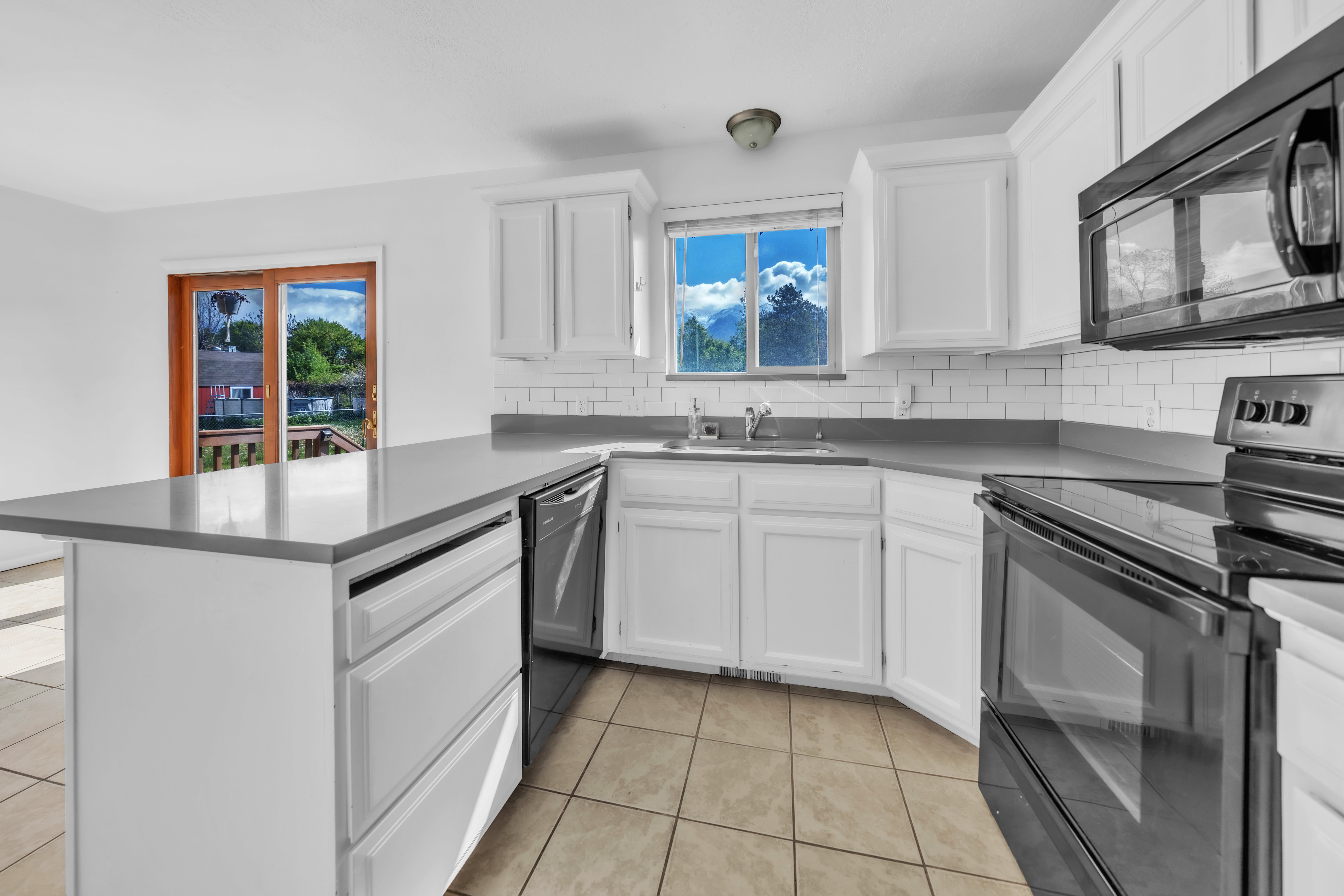 Kitchen with black appliances, white cabinets, a peninsula, light tile patterned floors, and backsplash