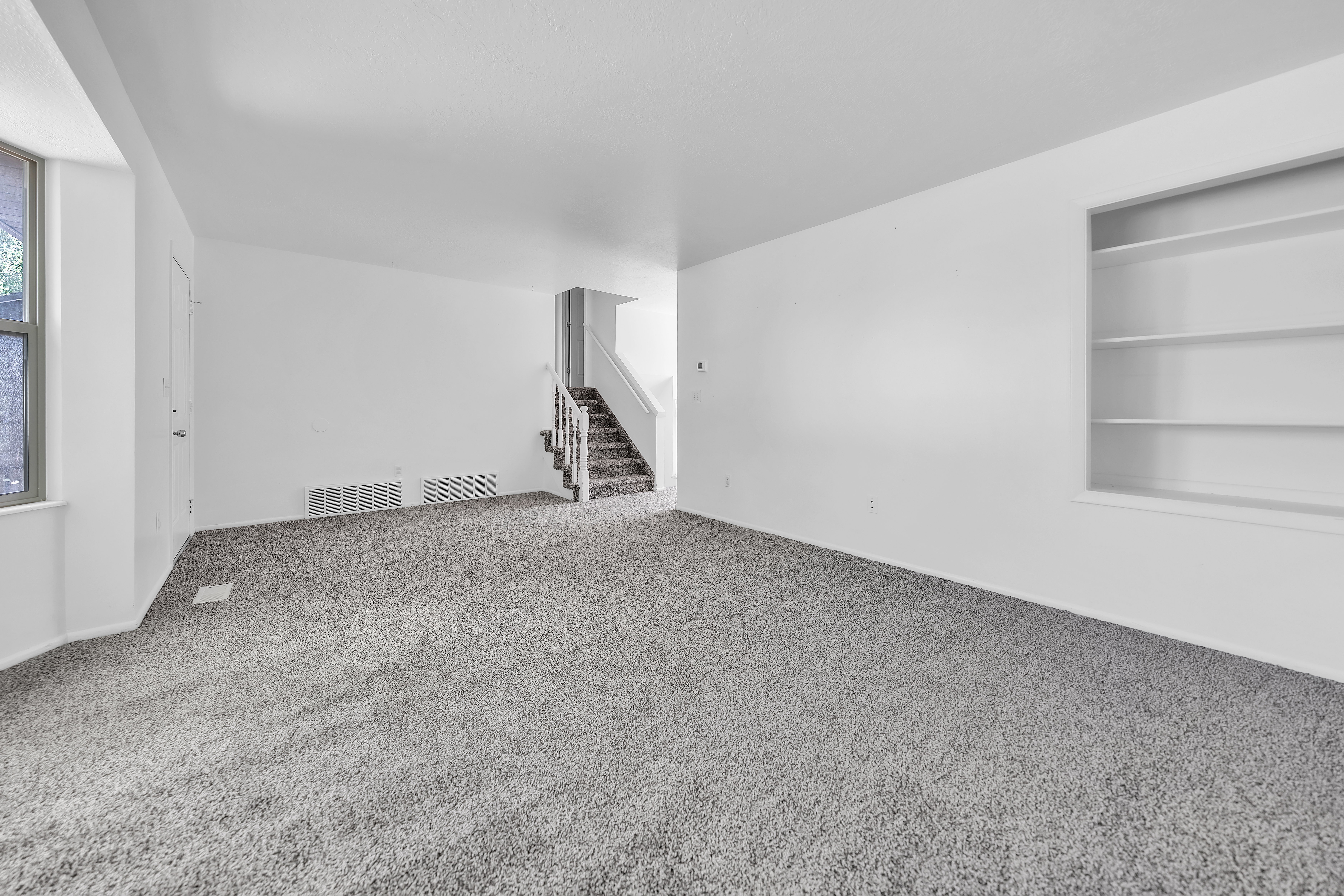 Spacious interior room featuring light grey carpet, white walls, and a prominent built-in shelving unit