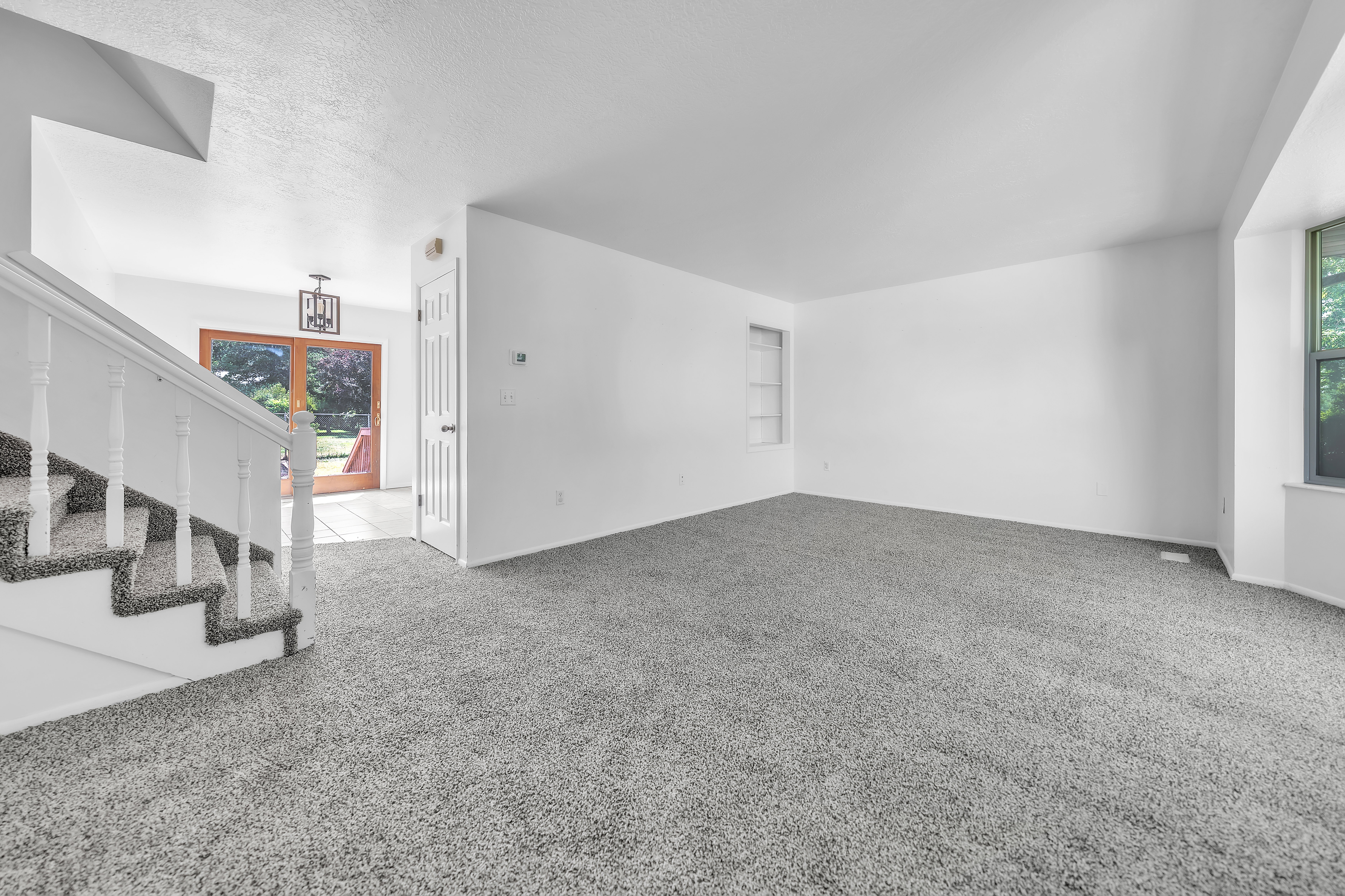 Spacious living area featuring grey carpeting, white walls, and a built-in shelving unit
