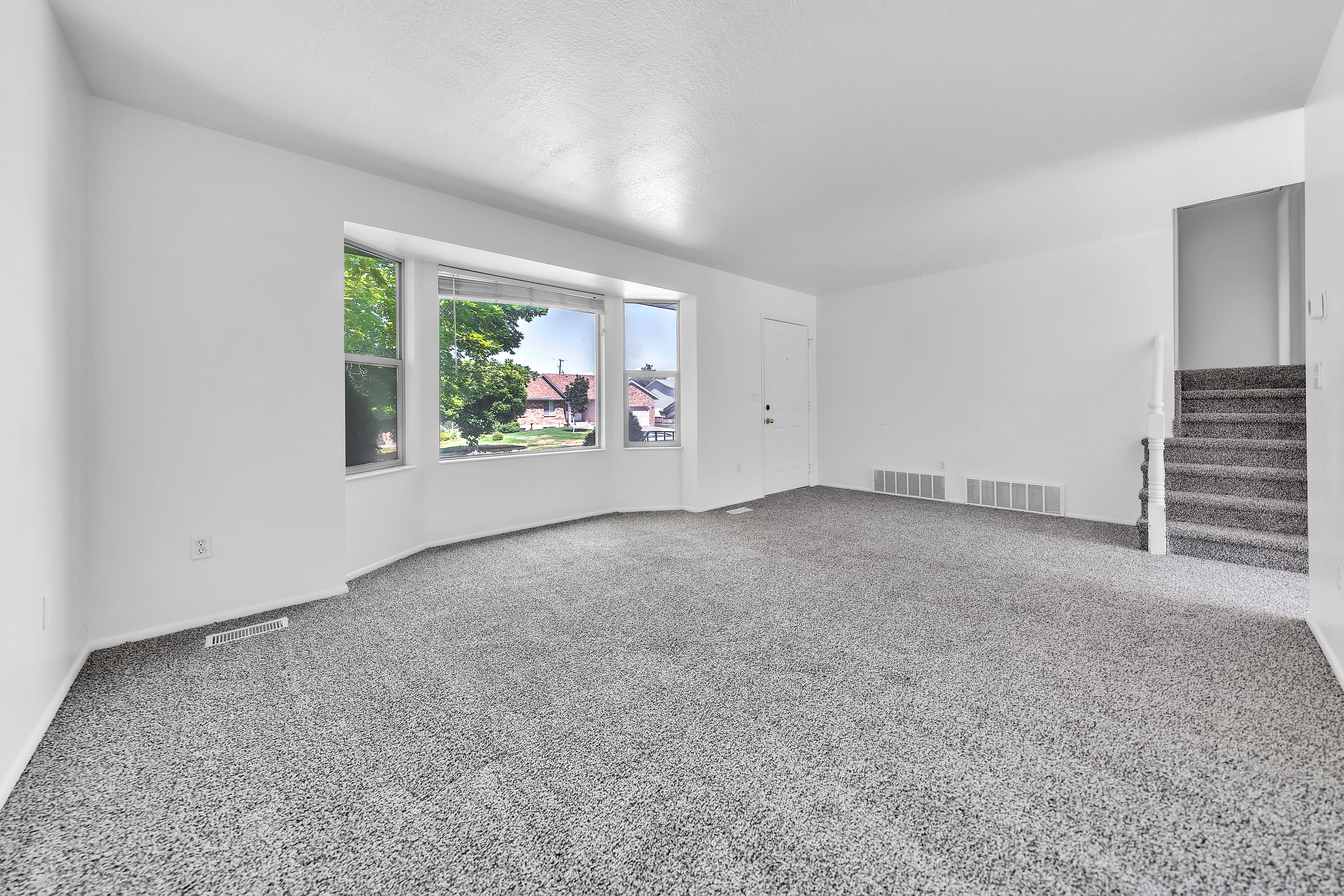 Expansive living space featuring light gray carpet, white walls, and a bay window with multiple panes